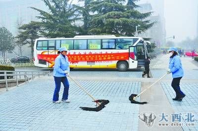  1月10日，济南市泉城广场，两名清洁工正在用拖布清洁地面，不远处是一献血车。 刘明照/CFP
